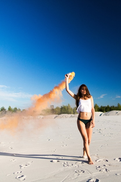 Woman walks with smoke on white beach under blue sky