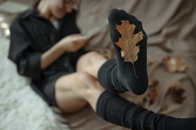 A woman in warm stockings on a blurred background and an autumn leaf in focus.