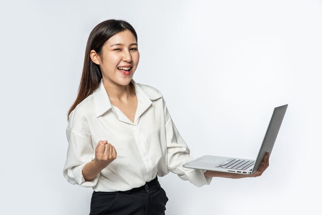 The woman was wearing a white shirt and dark pants, holding a laptop, and pretending to be joyful