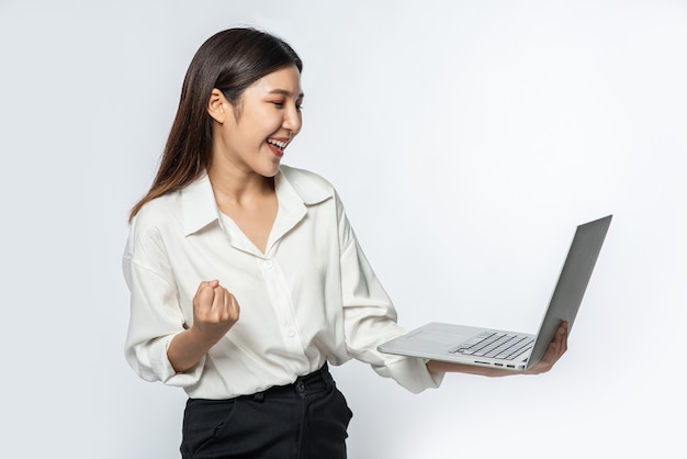 The woman was wearing a white shirt and dark pants, holding a laptop, and pretending to be joyful