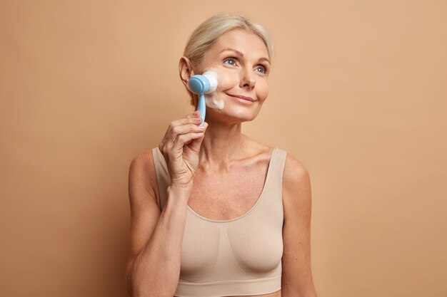 woman washes face with brush and cleansing foam takes care of complexion skin