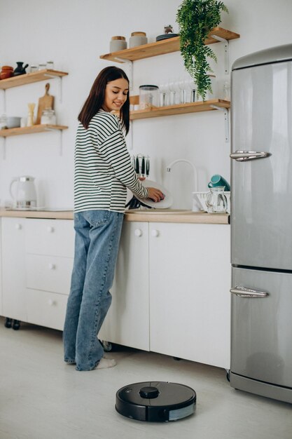 film Deter Geniet Free Photo | Woman washing dishes while robot vacuum cleaner tidying up the  house