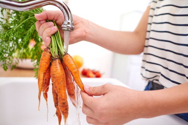Женщина моет свежую и органическую морковь