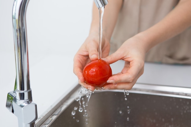 Woman washing tomato with tap water