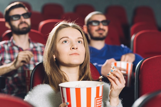 Женщина смотрит фильм в кино рядом с мужчинами