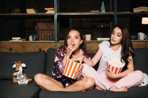 Женщина смотрит фильм, пока ее друг берет попкорн из своего ведра