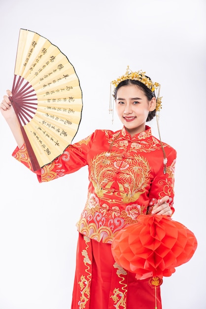 Foto gratuita la donna indossa il vestito cheongsam tiene il ventaglio cinese e la lampada rossa per mostrare il grande evento nel capodanno cinese