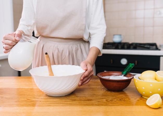 Woman wearing apron preparing cake in kitchen with ingredients on table