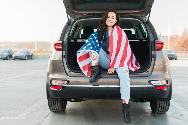 Woman wearing big usa flag in car trunk