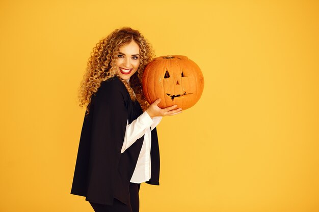 Woman wearing black costume. Lady with halloween makeup. Girl standing on a yellow background.