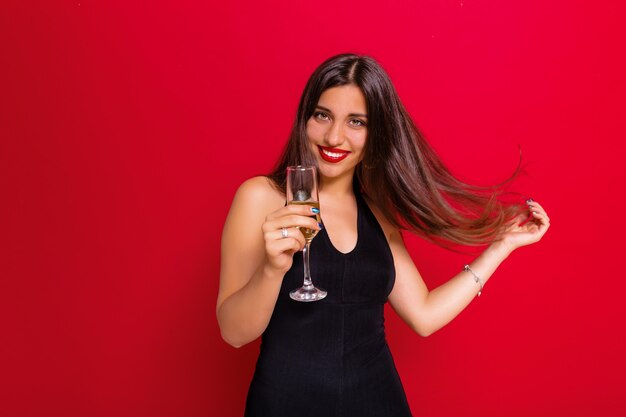 woman wearing a black dress and holding a champagne glass posing on red