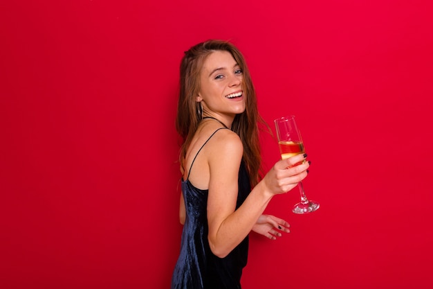 Donna che indossa un abito nero e che tiene un bicchiere di champagne in posa sul rosso