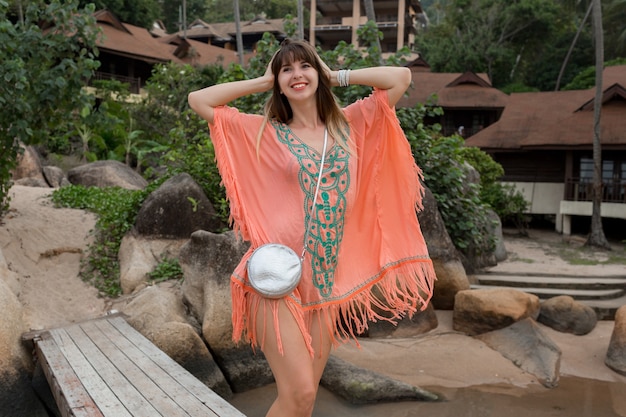 해변에 산책하는 Boho 드레스를 입고 여자. 바위와 배경에 palmtrees입니다. 여름 패션.