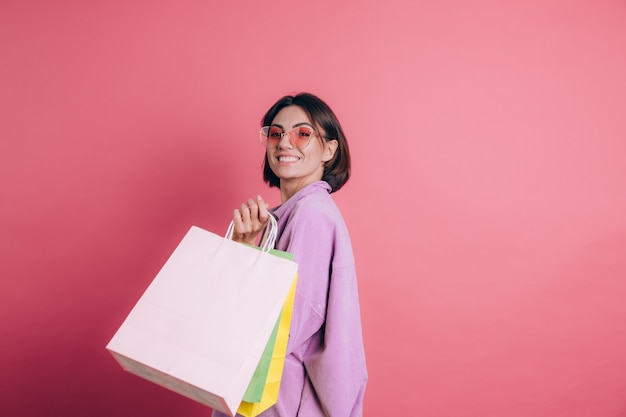 Женщина в повседневном свитере на фоне счастливой, наслаждаясь покупками, держа красочные сумки в летних солнцезащитных очках