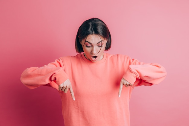 Woman wearing casual sweater on background pointing down with fingers showing advertisement, surprised face and open mouth