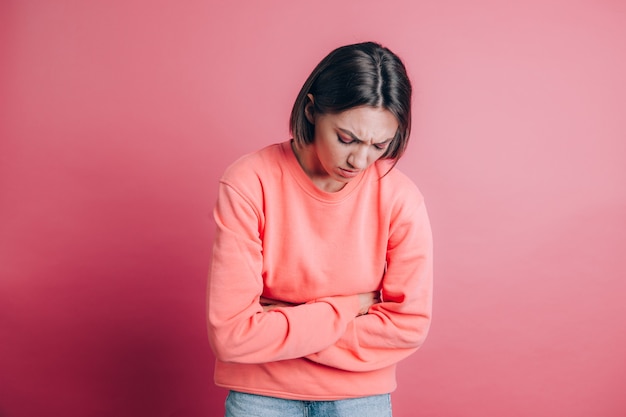 Donna che indossa un maglione casual su sfondo che soffre di mal di stomaco con smorfia dolorosa, sensazione di crampi mestruali improvvisi, concetto di ginecologia