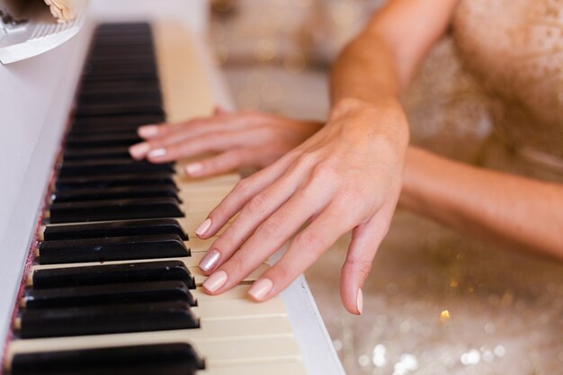 Woman wearing evening shiny golden christmas dress playing piano at home.