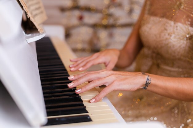 Woman wearing evening shiny golden christmas dress playing piano at home.