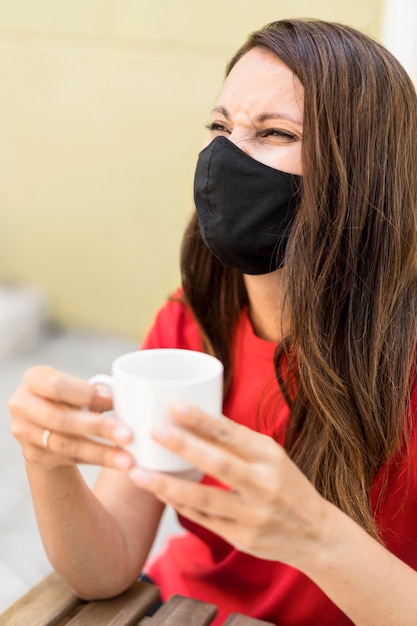 Donna che indossa la maschera in tessuto e che tiene una tazza di caffè