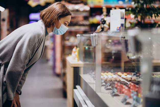 Donna che indossa la maschera per il viso e lo shopping nel negozio di alimentari