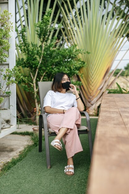 Woman wearing a face mask sitting on a chair beside a swimming pool in the garden.