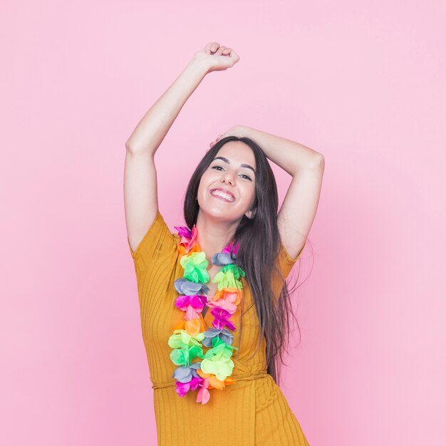 Woman wearing fake colorful garland around her neck dancing against pink background