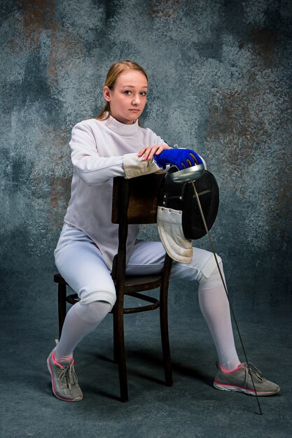 The woman wearing fencing suit with sword against gray