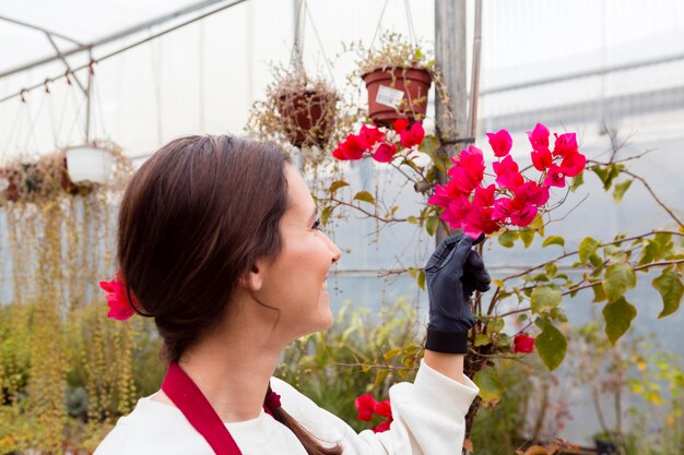 Woman wearing gardening clothes and touching flowers in greenhouse