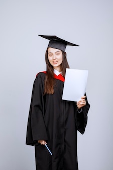 Женщина в выпускной кепке и церемониальной мантии держит пустые документы. фото высокого качества