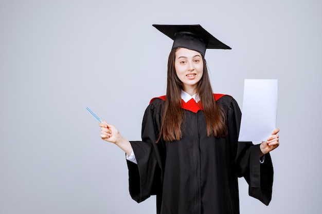 Woman wearing graduation cap and ceremony robe holding empty papers. High quality photo