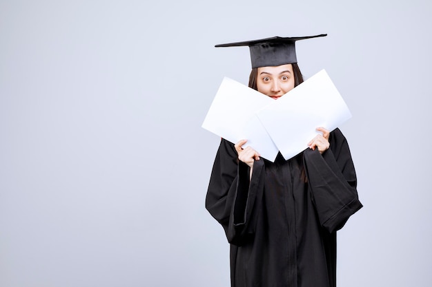 Donna che indossa cappello di laurea e abito da cerimonia che mostra documenti vuoti. foto di alta qualità