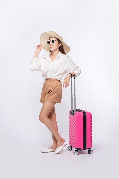 旅行に帽子、眼鏡、スーツケースのハンドルを身に着けている女性