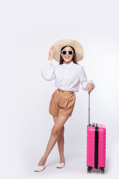 旅行に帽子、眼鏡、スーツケースのハンドルを身に着けている女性