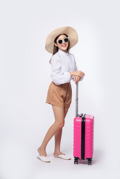 Woman wearing a hat, glasses, and handles of suitcases to travel