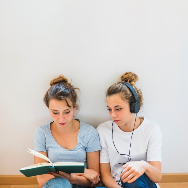 Woman wearing headphone looking at friend reading book