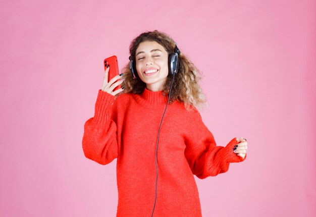 woman wearing headphones listening to her playlist at smartphone and dancing.