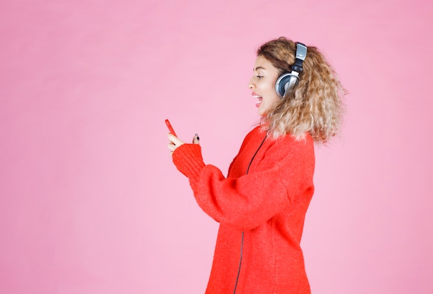 woman wearing headphones listening to her playlist at smartphone and dancing.