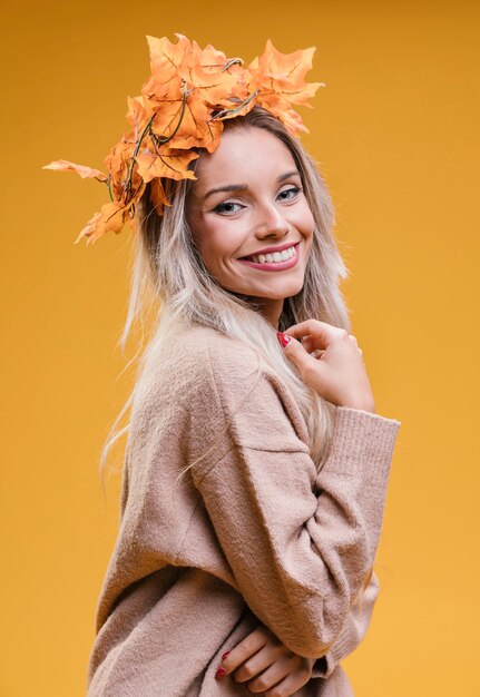 Woman wearing maple leaves tiara posing against yellow wall