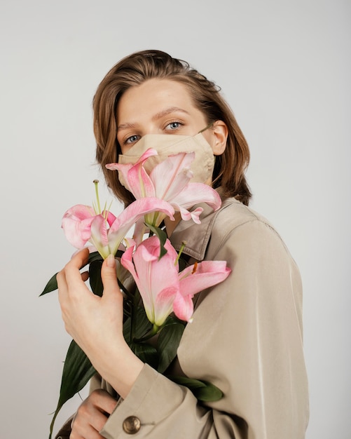 Foto gratuita donna che indossa una maschera e azienda bouquet di fiori