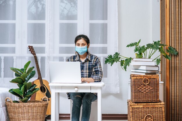 마스크를 쓰고있는 여자 위생은 노트북과 함께 책상에 앉아있다.