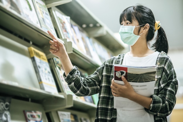 A woman wearing a mask and searching for books in the library.