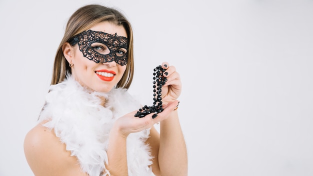 Woman wearing masquerade carnival mask holding necklace over white background