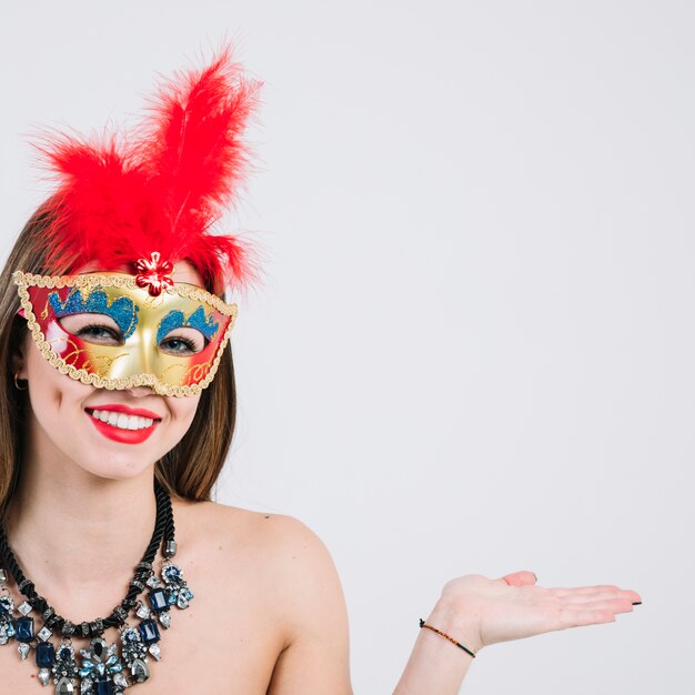 Woman wearing masquerade carnival mask and necklace gesturing over white backdrop