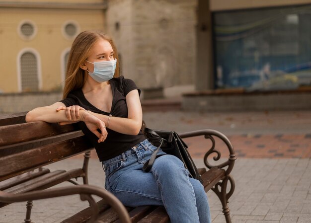 Woman wearing a medical mask outside while sitting on a bench