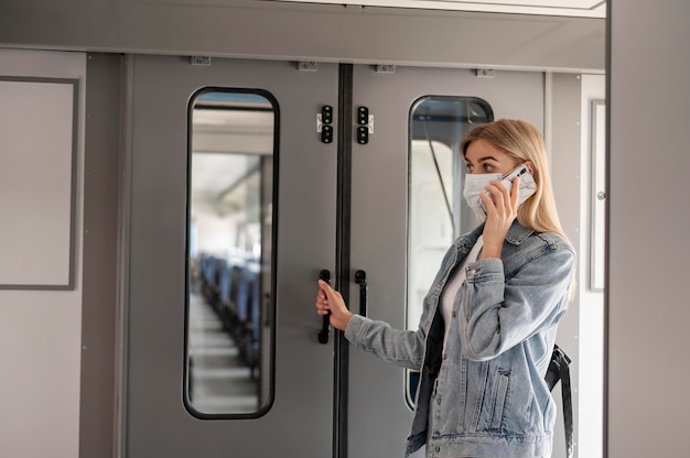 電車で旅行の準備をしながら、医療用マスクを着用し、電話で話している女性
