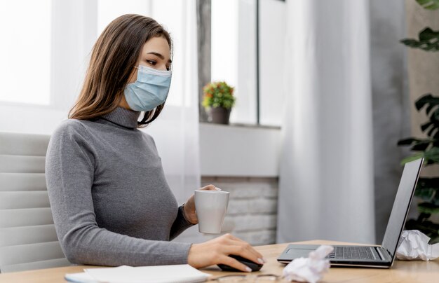 Donna che indossa una maschera medica mentre si lavora da casa