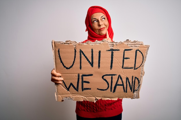 Foto gratuita donna che indossa l'hijab musulmano che chiede lo striscione della tenuta del sindacato con il messaggio di supporto unito faccia seria che pensa alla domanda idea molto confusa