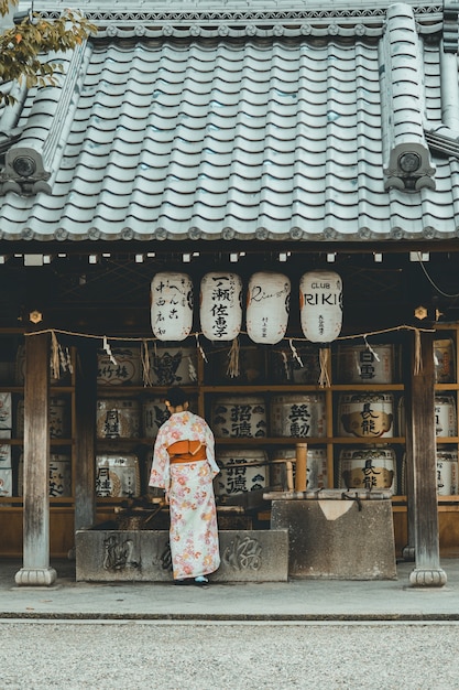 Foto gratuita donna che indossa un abito kimono arancione e bianco in piedi vicino alla casa