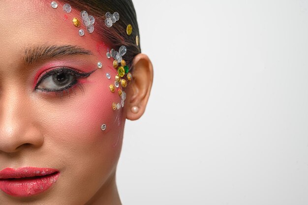 Woman wearing pink makeup and embellishments on her face isolated on white