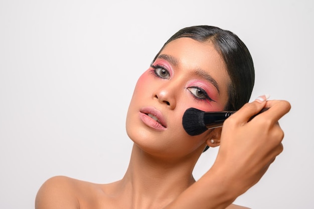 Woman wearing pink makeup and holding a blush brush isolated on white